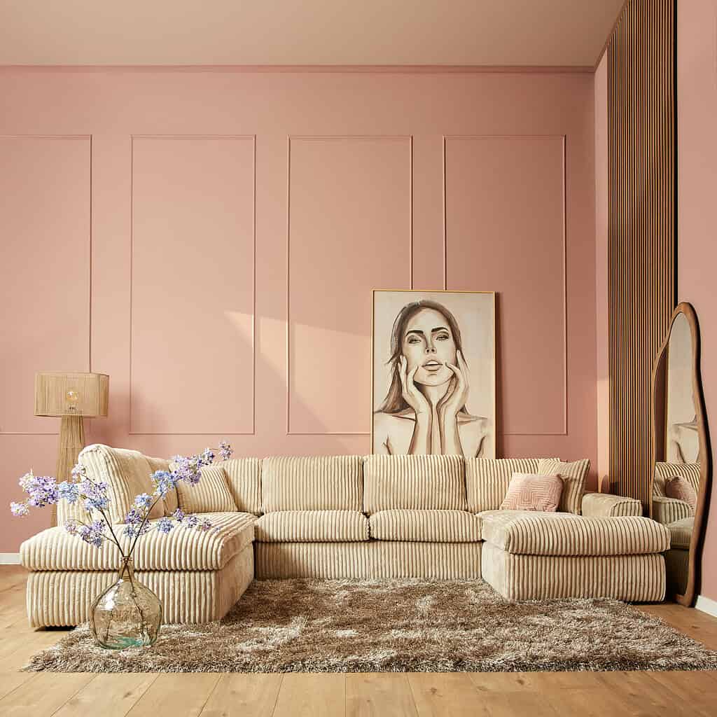 Lichte vintage bank in beige corduroy stof met strak design, comfortabele zithoek en decoratieve elementen zoals een grote spiegel en kunstzinnig portrait op een roze muur.