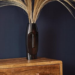 Unieke houten Afrikaanse maskersculptuur met natuurlijke uitstraling op houten kast, perfecte decoratie voor modern en eclectisch interieur.