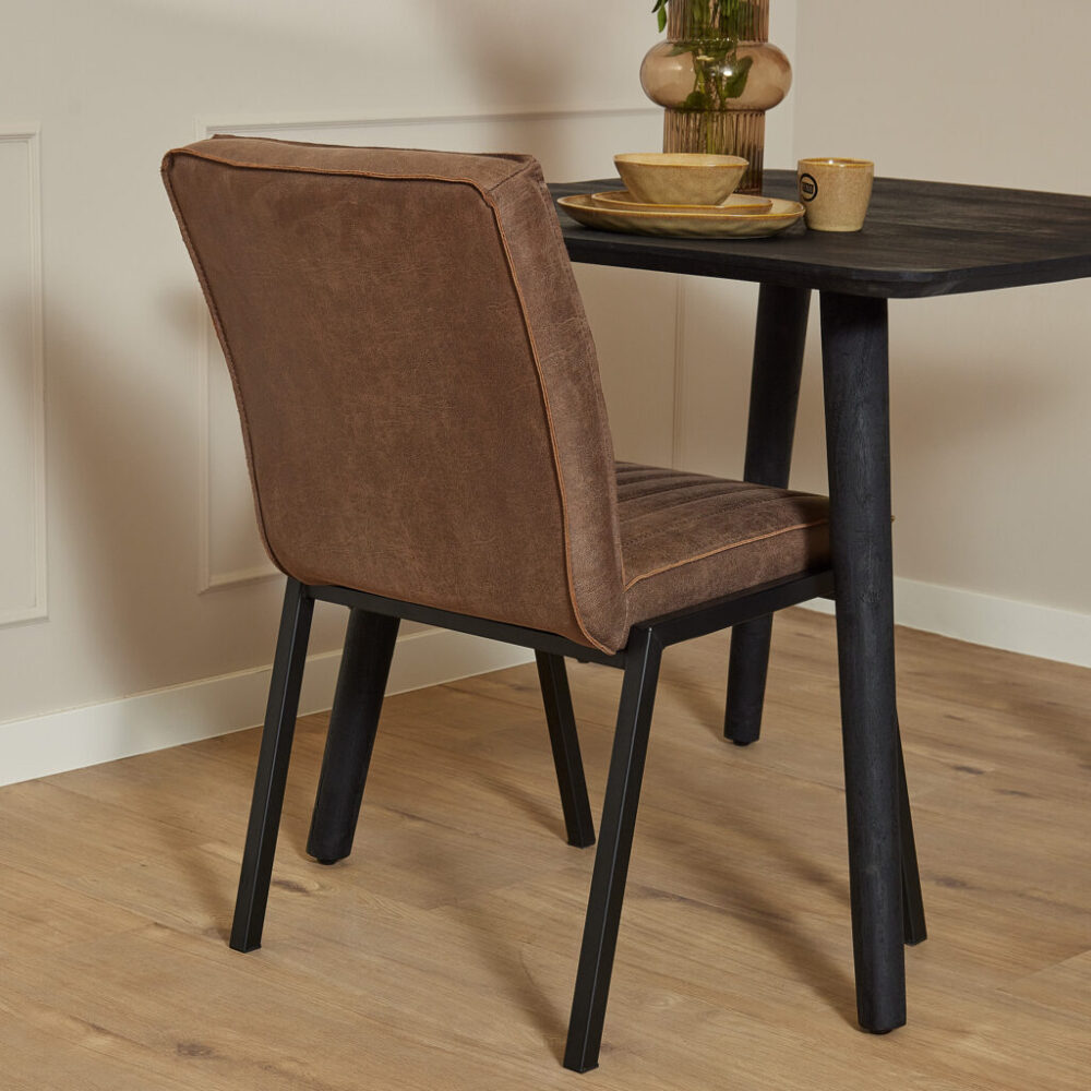 Zwarte eettafel met houten tafelblad en stoere zwarte poten, gecombineerd met een vintage bruine leren eetkamerstoel exclusief design, perfect voor moderne woonruimtes.