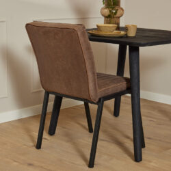 Zwarte eettafel met houten tafelblad en stoere zwarte poten, gecombineerd met een vintage bruine leren eetkamerstoel exclusief design, perfect voor moderne woonruimtes.