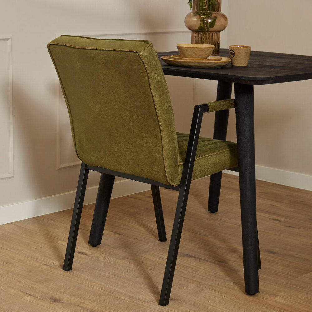 Oud groene velvet eetkamerstoel met zwart metalen frame en houten tafel met decoratief interieur.