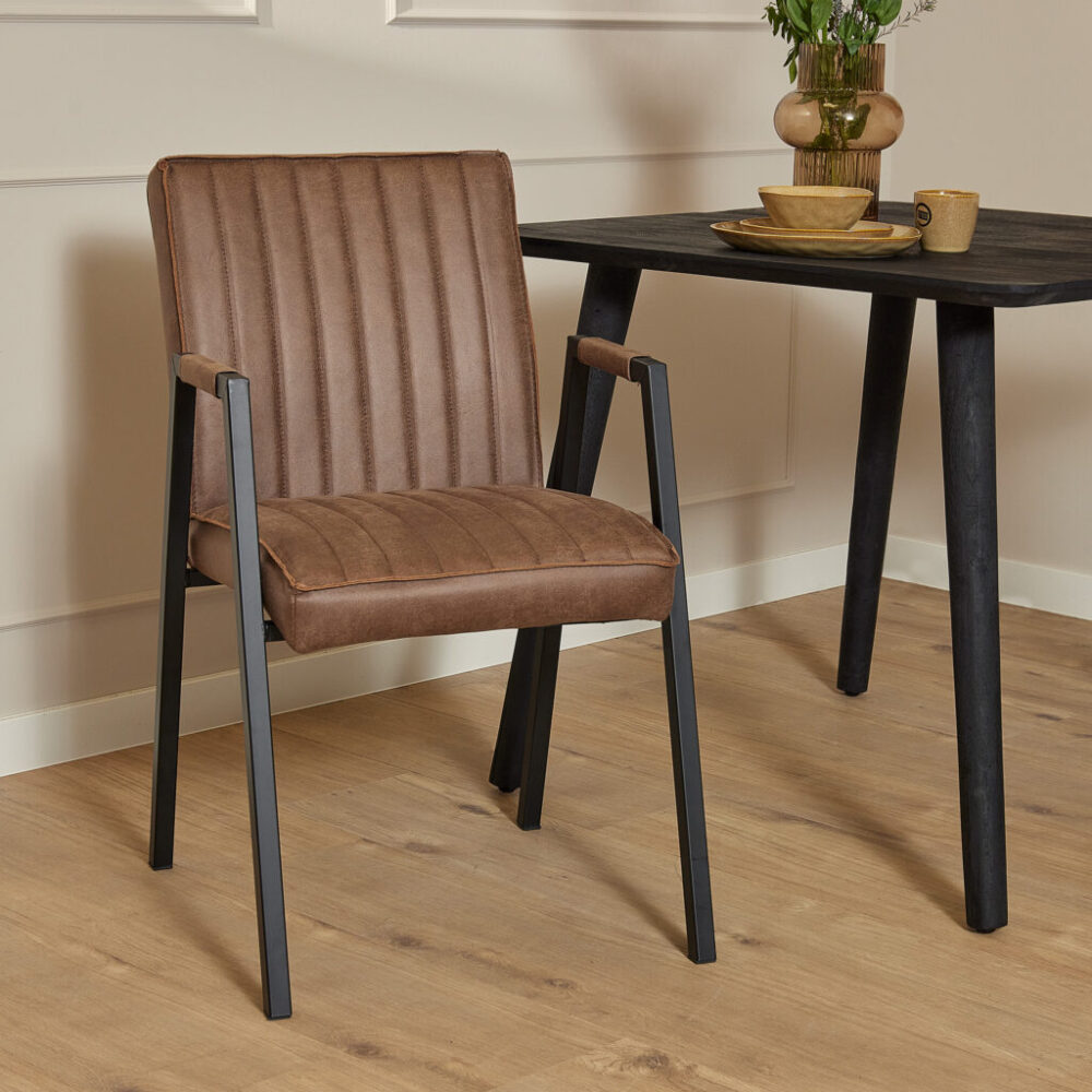 Zitstoel met leren bekleding en metalen frame naast een donker houten eettafel, geschikt voor modern interieur en eetkamermeubels van Mokana Meubelen.