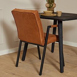 Elegante leren eetkamerstoel met zwarte metalen poten, perfect voor een modern en warm interieur, gecombineerd met een donker houten eettafel en stijlvolle accessoires.