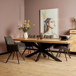 Großer Esstisch aus Holz mit schwarzem Metallgestell, umgeben von vier Teppichstühlen in einem modernen Interieur, dekorative Vase mit Blumen und ein buntes Kunstwerk an der Wand.