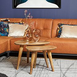 Kleine houten bijzettafels met glazen vazen en decoratieve takken, in een gezellige woonkamer met leren bank en kleurrijke kussens, perfect voor een stijlvolle interieurafwerking.