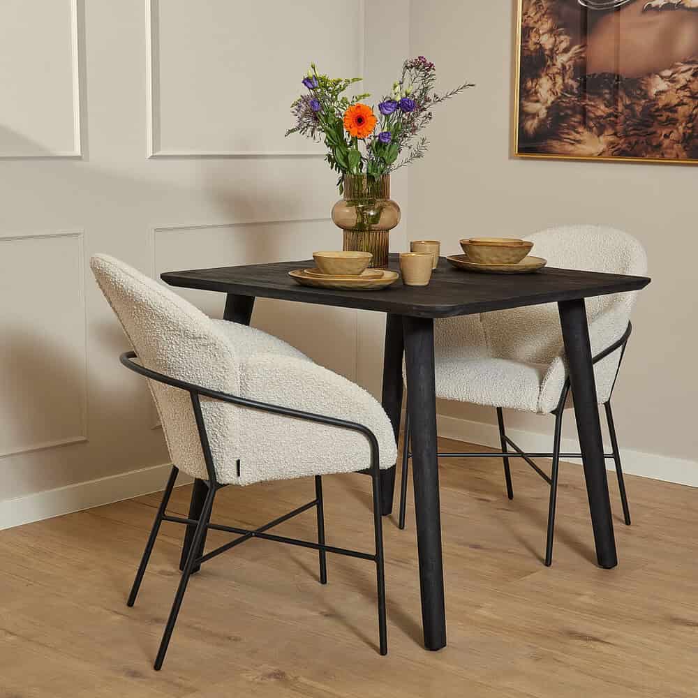 Eettafel met zwarte houten poten en twee witte stoffen armstoelen, gecombineerd met een bloemenvaas met kleurrijke bloemen, geschikt voor een stijlvolle en gezellige woonkamer inrichting.