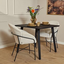 Eettafel met zwarte houten poten en twee witte stoffen armstoelen, gecombineerd met een bloemenvaas met kleurrijke bloemen, geschikt voor een stijlvolle en gezellige woonkamer inrichting.