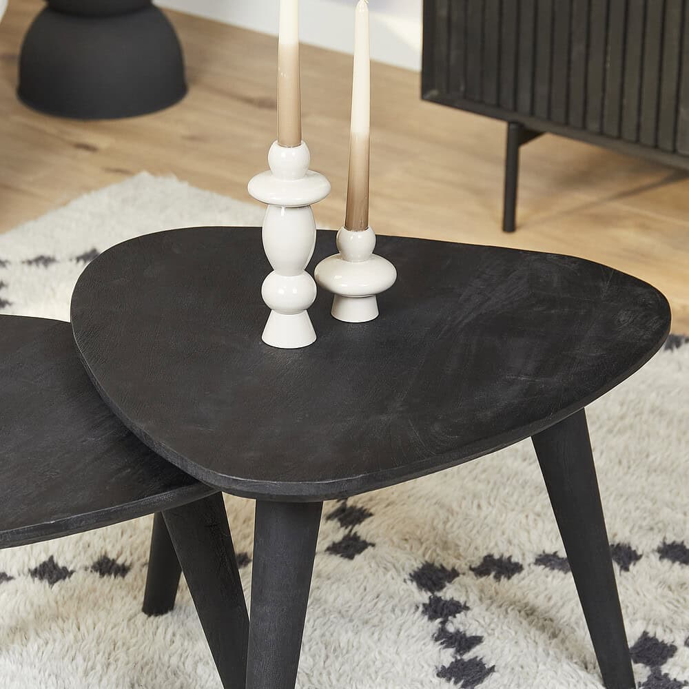 Gestileerde zwarte houten salontafels met moderne uitstraling, afgewerkt met gezellige accessoires zoals witte kandelaars, in een sfeervolle woonkamer.