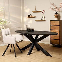 Moderne eettafel met zwart metalen onderstel en ovaal massief houten blad, gecombineerd met een zachte, geborduurde eetkamerstoel, perfect voor een eigentijdse interieurstijl.