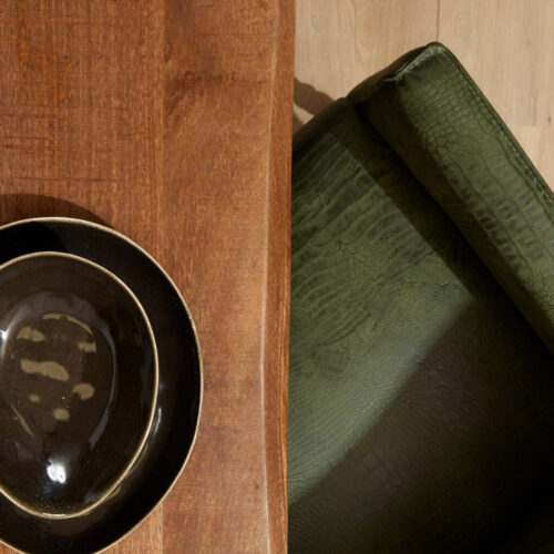 Eclectische houten tafel gecombineerd met een groen leren fauteuil, perfect voor modern interieur en comfort. Elegante meubelstukken die stijl en functionaliteit combineren.