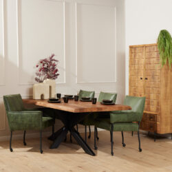 Rustieke eettafel met massief houten blad en zwart metalen onderstel, ronde zwarte servies en groene velvet eetkamerstoelen in modern interieur.