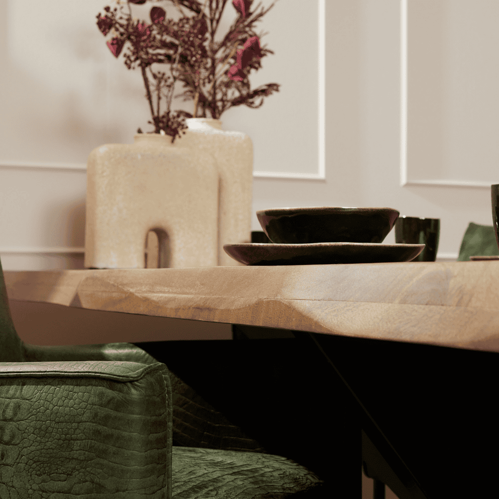 Unieke houten eettafel met natuurlijke afwerking, gecombineerd met keramische borden en een sfeervolle muurbloem in decoratieve vazen voor een moderne en stijlvolle eetkamer.