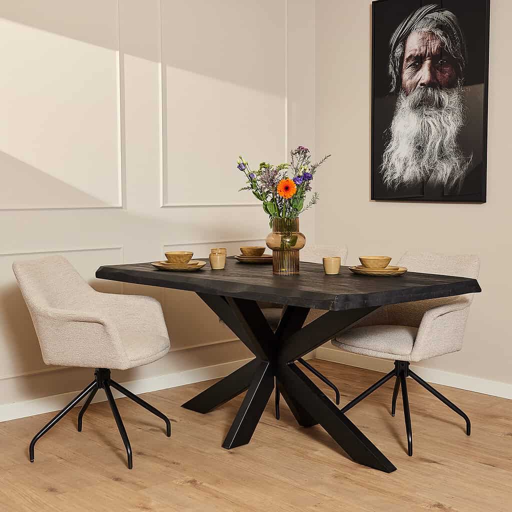 Uniek houten eettafel met zwart onderstel en comfortabele beige eetkamerstoelen, stijlvol gedekt met bloemen en servies, in een moderne eetkamer met elegant wandpaneel en foto van een oude man, perfect voor landelijke en Scandinavische interieurstijlen.