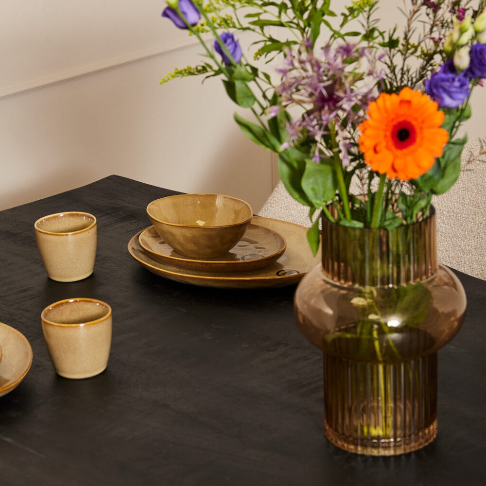 Vaas met zomerbloemen op een donker houten eettafel in een modern interieur.
