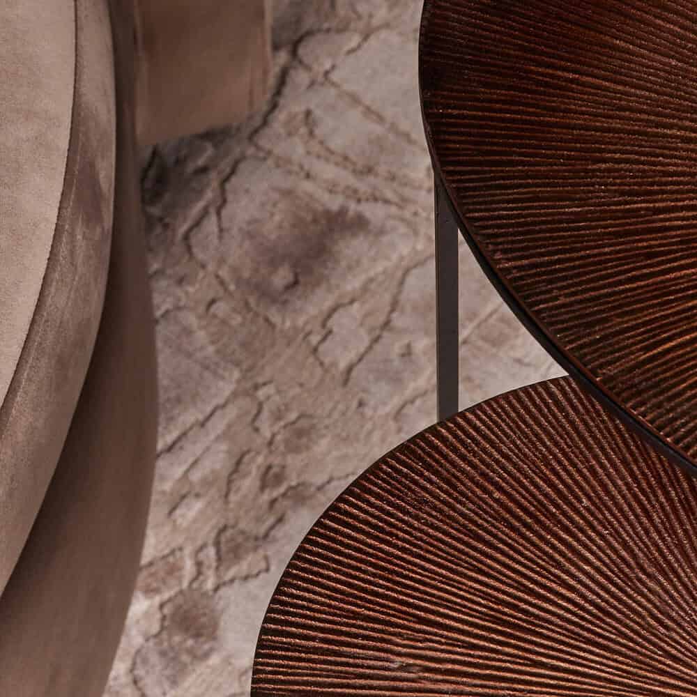 Sfeervolle close-up van een elegante, ronde houten tafel met structuur en warme afwerking, onderdeel van de Mokana Meubelen collectie voor stijlvolle interieurs.