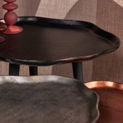 Rauw houten en metalen serveerbladen in zwart, grijs en koperkleur op een houten en stoffen achtergrond.