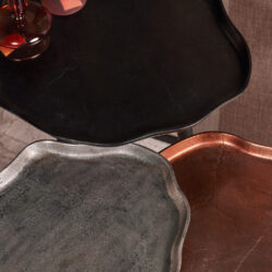 Grote zwart marmeren bijzettafel met afgeronde randen, stijlvolle eetkast, en rustieke koperen schaal, perfect voor moderne en industriële interieurdecoratie.