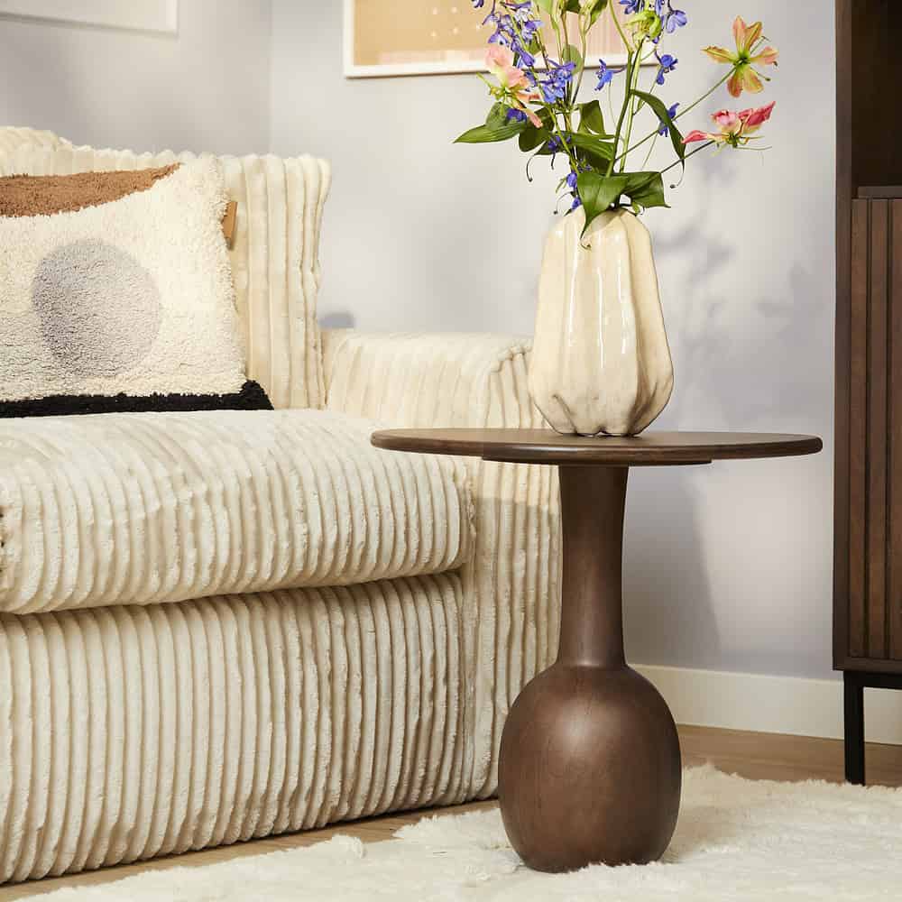 Met deze foto van een stijlvolle woonkamer met een beige gestoffeerde bank en een natuurlijke houten bijzettafel, benadrukken we de hoogwaardige meubelcollectie van Mokana Meubelen, inclusief comfortabele zitmeubelen en eigentijdse interieuraccessoires.