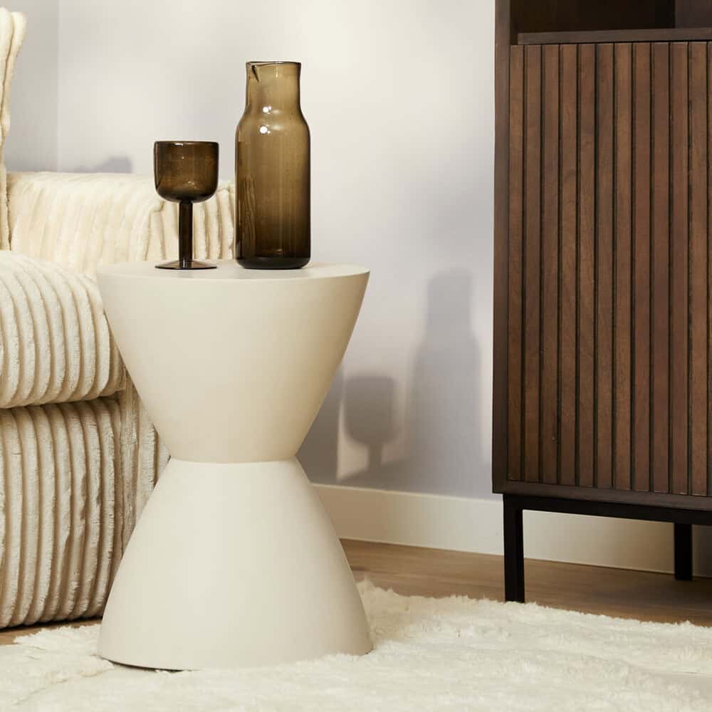Minimalistische bijzettafel met sierglazen op een eigentijdse woonkamer, gecombineerd met een velvet bank en een houten dressoir voor een warme, stijlvolle sfeer.