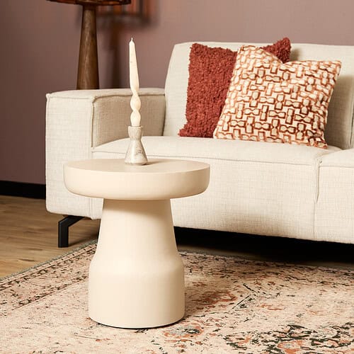 Elegant beige bijzettafel in modern design, ideaal voor woonkamer decoratie en accessoires, gecombineerd met gestileerde kussens en een sierlijke kaars op een prachtig tapijt.