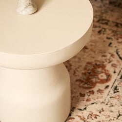 Stijlvolle witte bijzettafel van Mokana Meubelen met een moderne, minimalistische uitstraling en een ronde vorm, geplaatst op een charmante vintage tapijt.