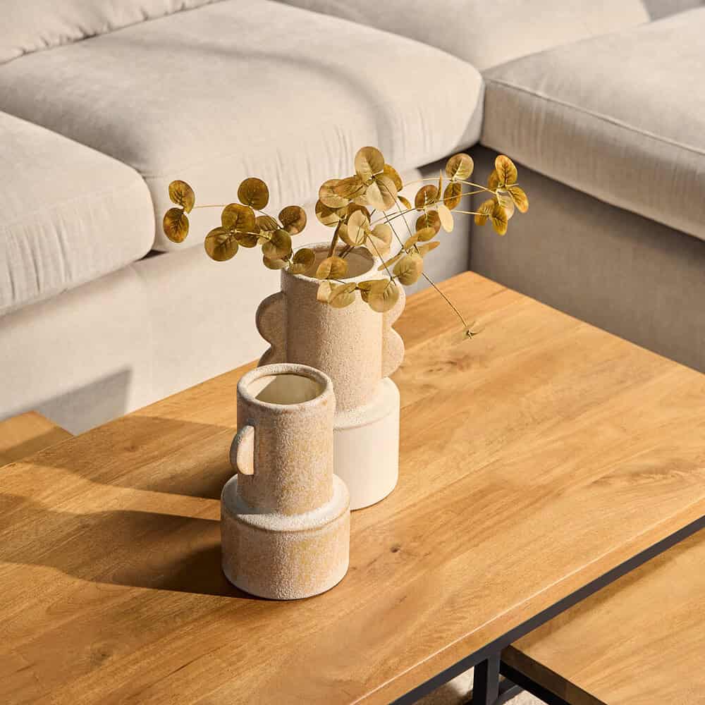 Moderne keramische vazen met eucalyptus tak, op houten salontafel in woonkamer met lichte bank.