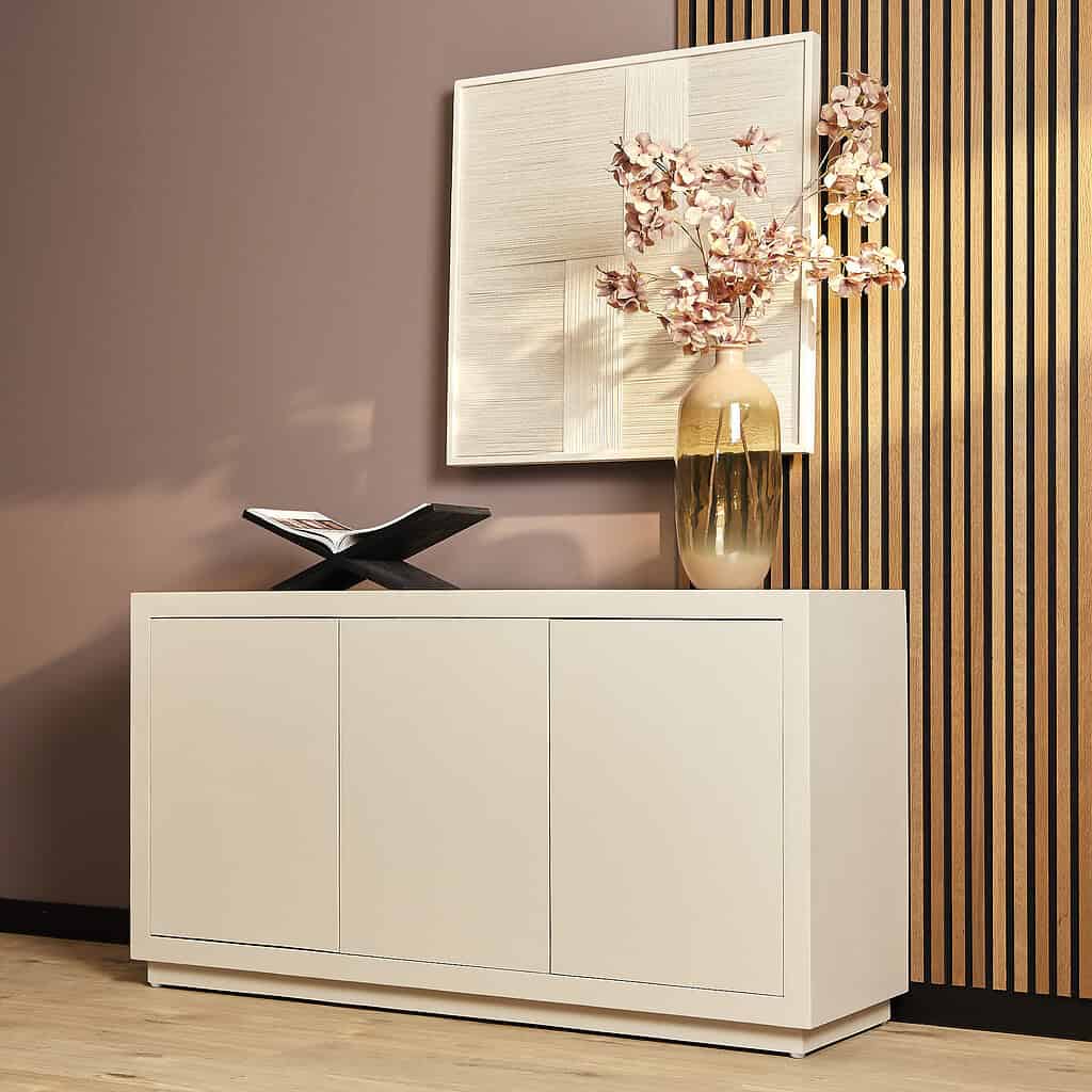 Strak witte buffetkast met bloemenvaas en kunstwerk in moderne woonkamer, design van Mokana Meubelen.