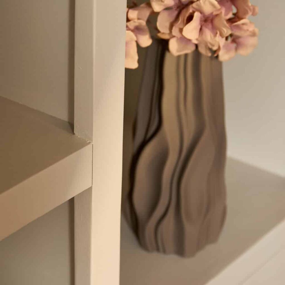 Houten meubel met strakke lijnen naast een vaas met bloemen in een modern interieur.