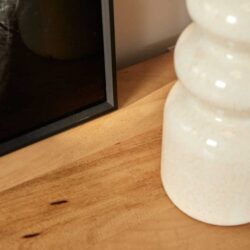 Houtkleurige houten meubel met donker glazen en keramische decoratie op een houten oppervlakte.