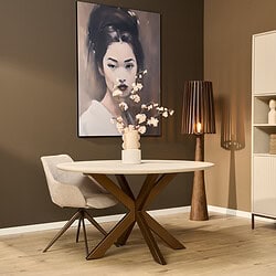 Modern eettafel met stoer houten onderstel en comfortabele vintage stoel naast een design tafellamp op een warme donkere muur met kunstwerk.