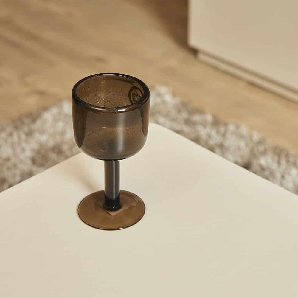 Gezellige donkere wijn- of cocktailglas op een witte tafel, in een interieur met zachte, warme uitstraling en houten vloer, perfect voor moderne en stijlvolle woonkamer of eetkamer.
