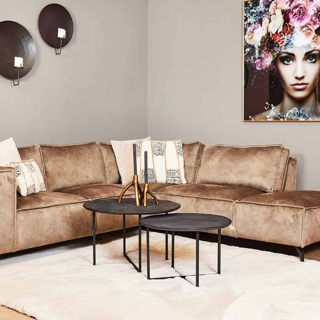 Houten bank met beige bekleding en modern zwart metalen salontafels, afgewerkt met decoratieve kandelaars en sierkussens, in een stijlvolle woonkamer met kunstwerk en wanddecoratie.
