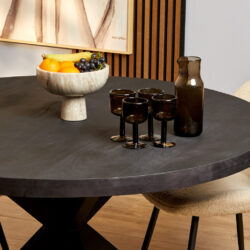 Elegant zwarte eettafel met bijpassende turquoise glazen en een schaal met vers fruit, in een moderne eetkamer met warme houten accenten en decoratieve kunst, perfect voor stijlvolle interieurdecoratie.