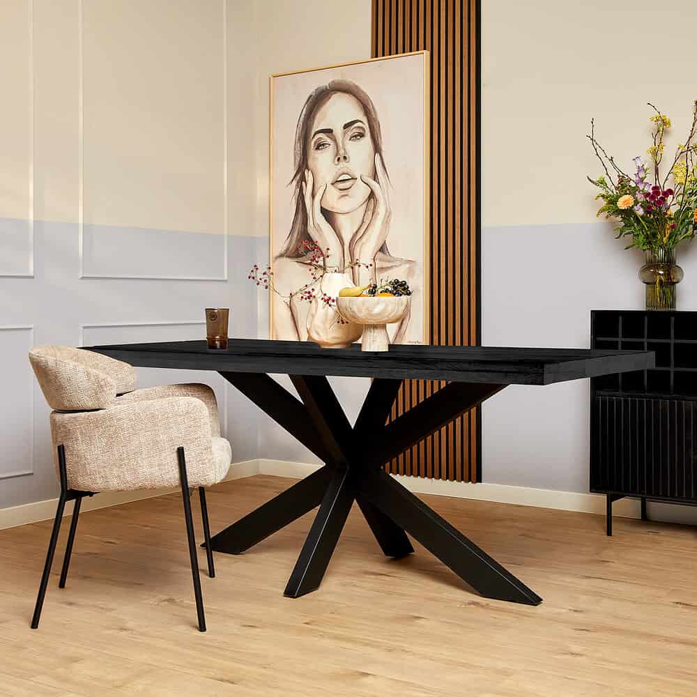 Black houten eettafel met een unieke X-vormige poten, modern interieur met kunstwerk en bloemen, ideaal voor stijlvolle eetruimtes.
