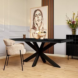 Black houten eettafel met een unieke X-vormige poten, modern interieur met kunstwerk en bloemen, ideaal voor stijlvolle eetruimtes.