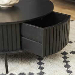 Strak zwart gelakt salontafel met lade, modern meubelstuk met verticale ribbels, ideaal voor woonruimte, op een witte en zwarte gestippelde tapijtvloer.