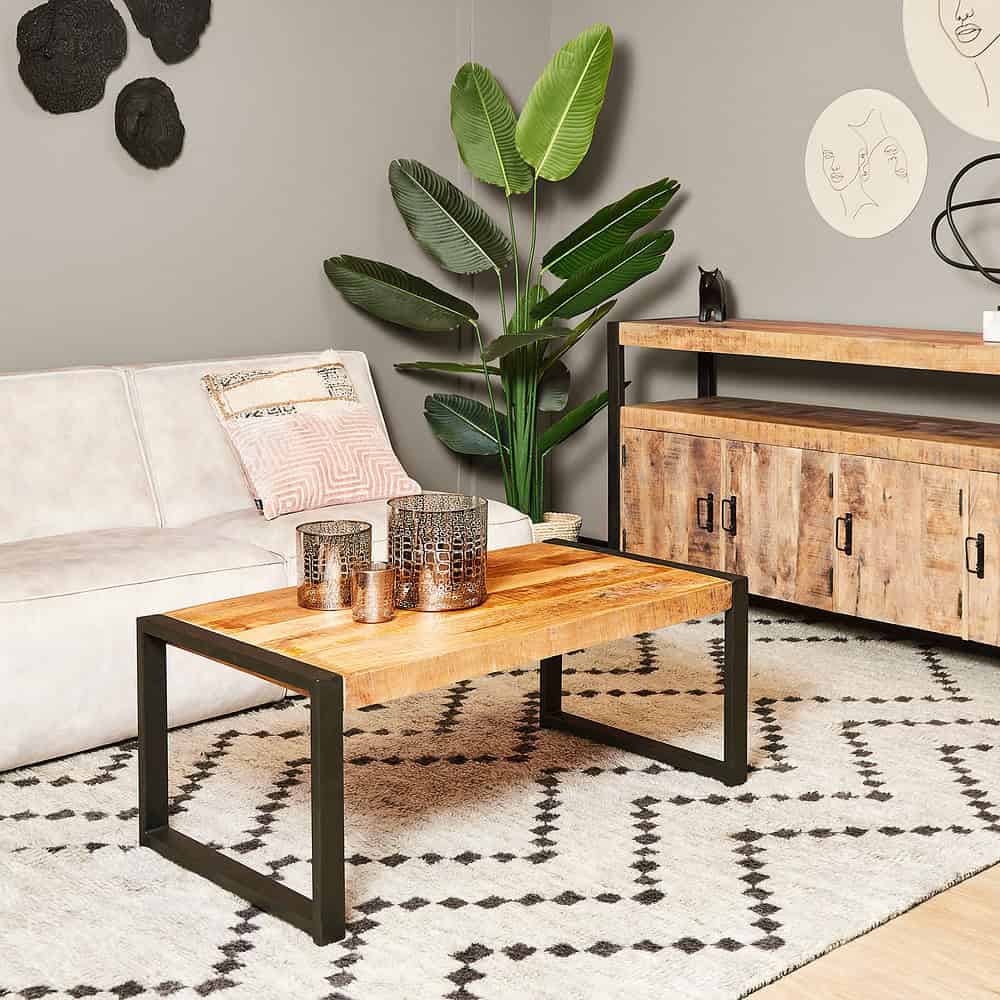Houten salontafel met zwart metalen frame in een modern woonkamer met beige bank, grote groene plant en decoratieve muurkunst. Perfect voor een stijlvolle en gezellige inrichting.