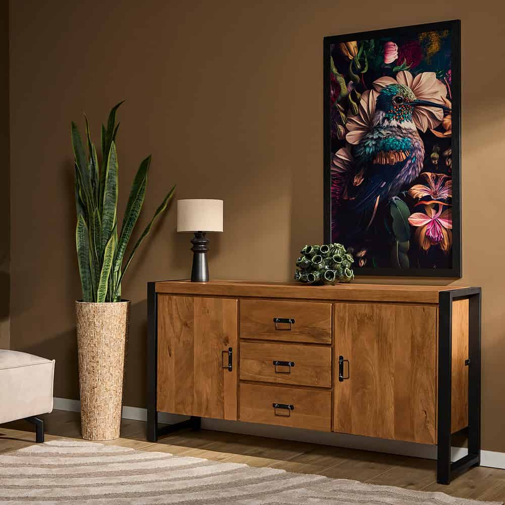 Een elegante houten dressoir met zwart metalen frame, gecombineerd met een royale kamerplant, tafelwaar, en een kleurrijk vogelkunstwerk, perfect voor een stijlvolle woonkamer.