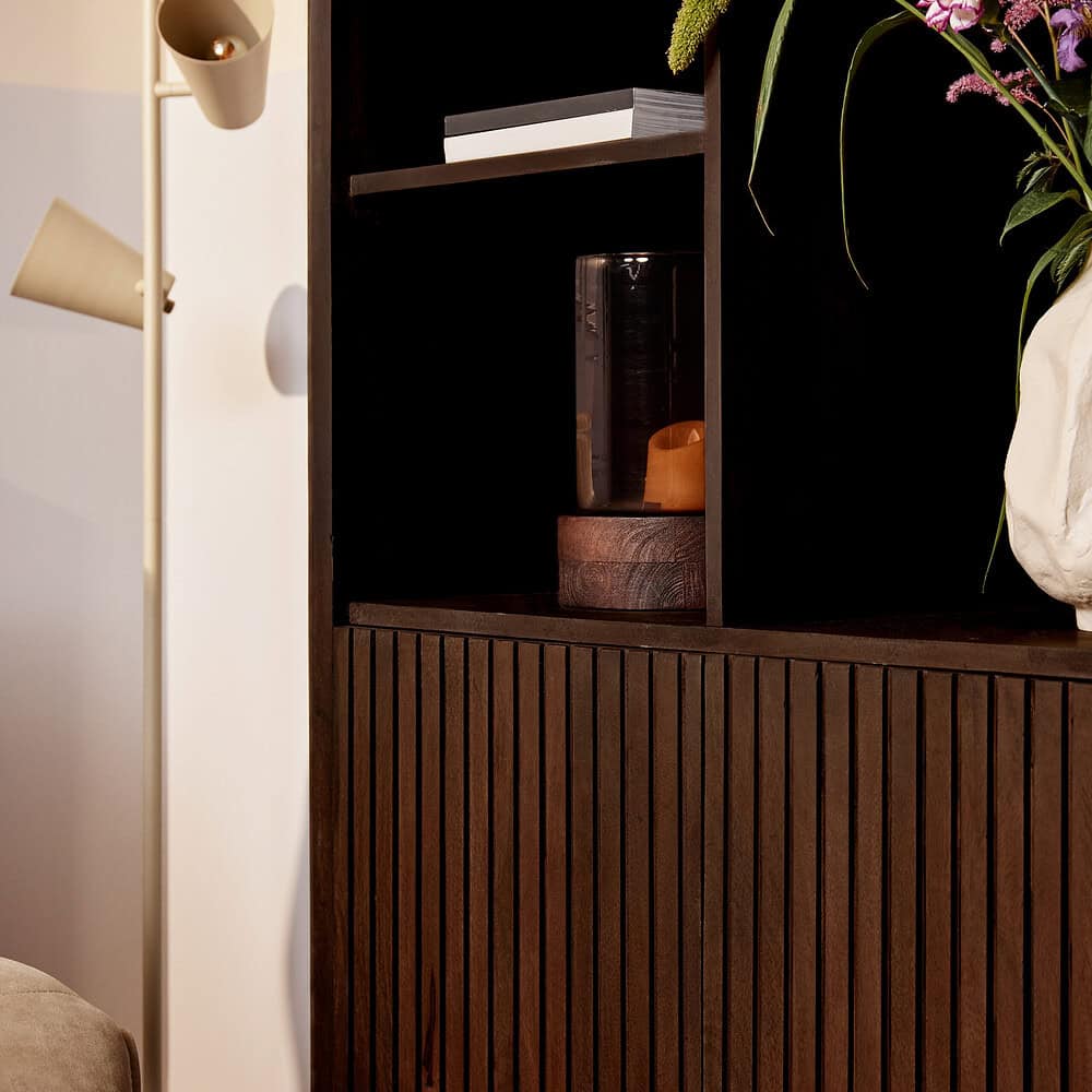 Groteelijke donkere houten boekenkast met verticale groeven en decoratieve accessoires, perfect voor modern interieur.