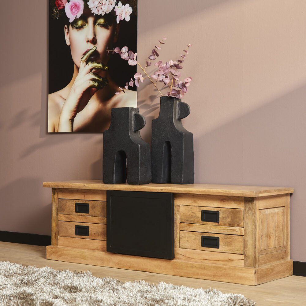 Robuuste houten tv-meubel met ladekasten en zwart metalen handgrepen, ideaal voor een landelijke of moderne woonstijl. Accessoires zoals zwarte keramieken vazen en kunstfoto maken het meubel compleet.