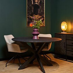 Grote houten eettafel met zwarte metalen X-poten, beige gestoffeerde lounge stoelen, kleurrijke bloemenvaas en sfeervolle lamp op een donkerhouten buffetkast in een moderne interieurstijl.