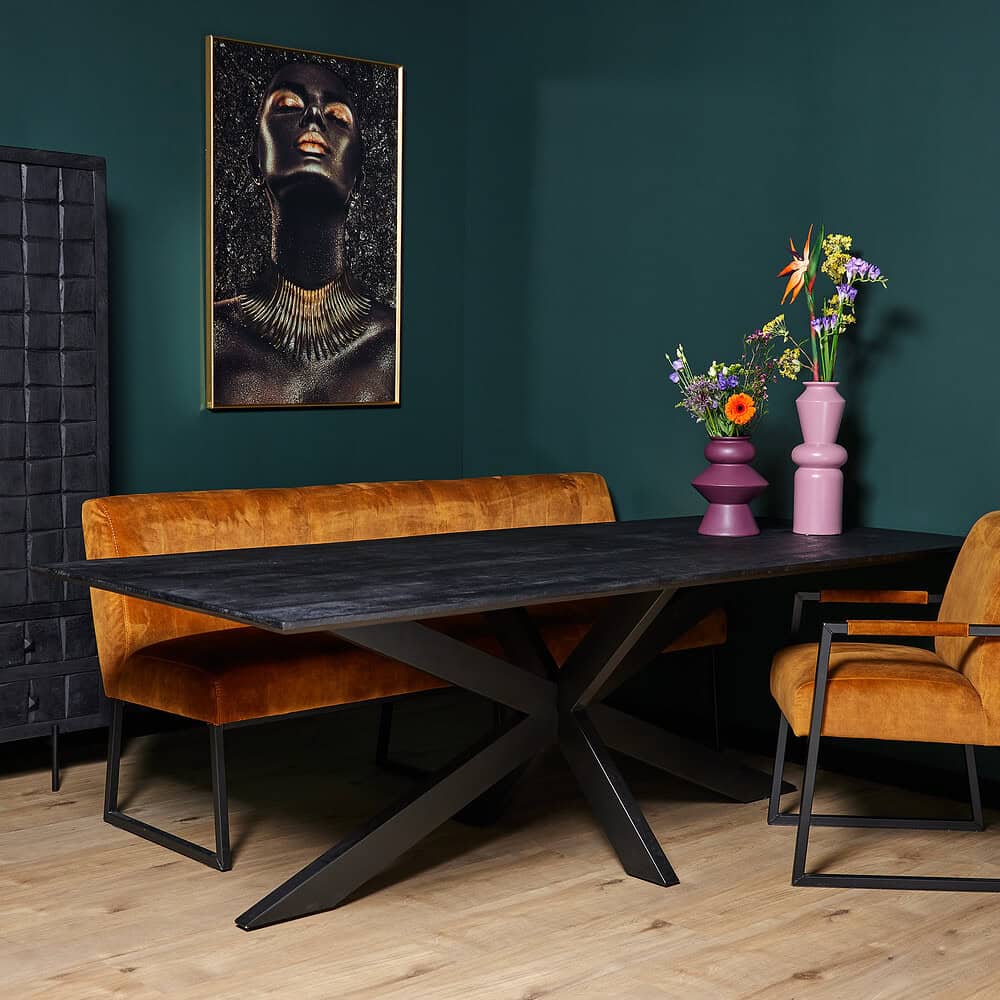 Elegante eettafel van zwart lengen hout met modern zwart metalen onderstel, gecombineerd met oranje velvet bank en stoel, sierlijke bloemenvazen en vibrerende muurkunst voor een stijlvolle interieurlook.