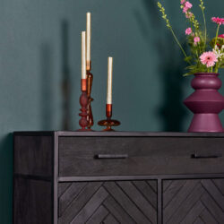 Kandelaar van gekleurd glas op zwart dressoir met bloemenvaas en roze bloemen, modern interieur accessoires, stijlvolle woondecoratie, elegant design meubels, Mokana Meubelen Nederland.