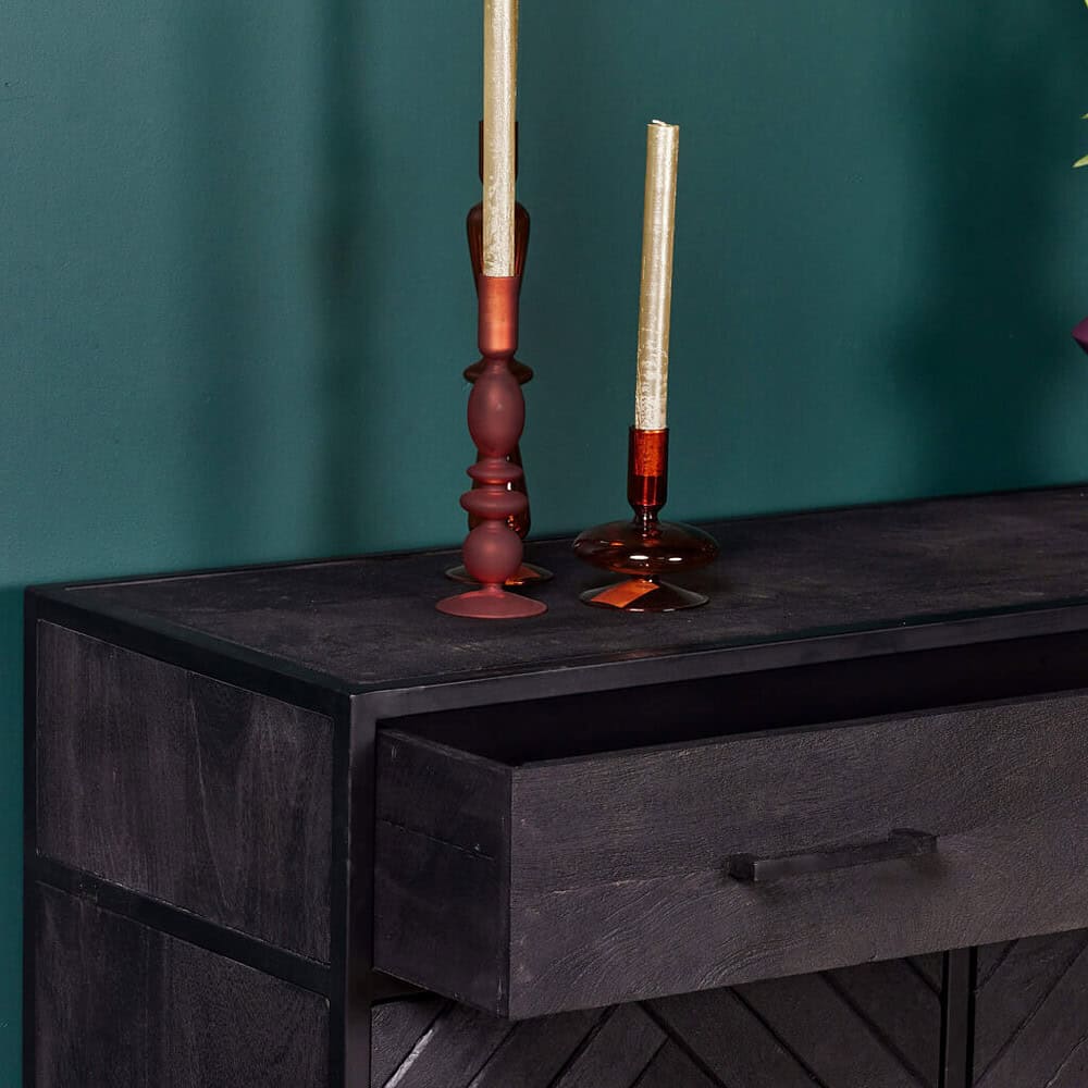 Stijlvolle zwarte houten dressoir met lade, decoratief met uniek gevormde sierkaarsen op een elegante groene muur achtergrond.