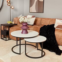 Mooie moderne salontafels met witte marmeren bladen en zwart metalen frames, gecombineerd met een zacht suède bank en stijlvolle decoratie voor een gezellige woonruimte.