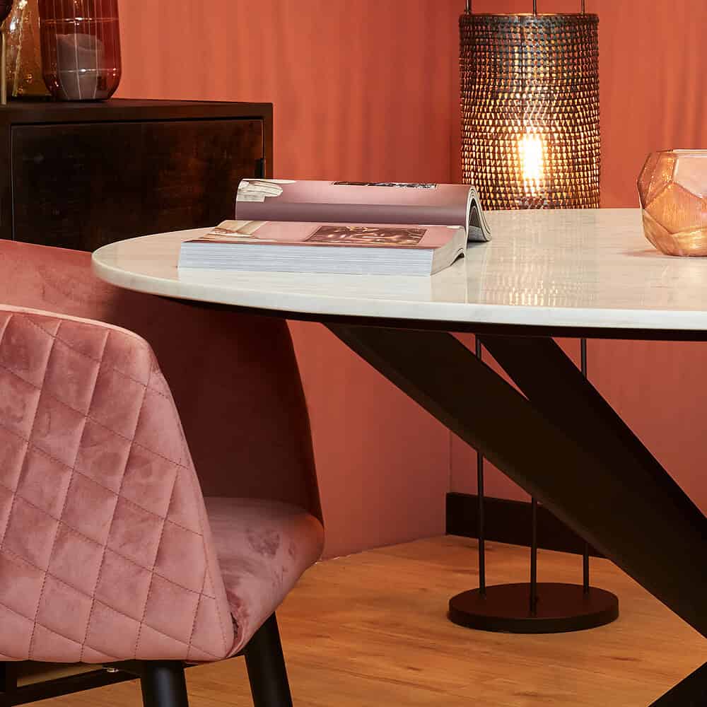 Elegant moderne eettafel met witte marmeren blad en zwart metalen onderstel,-vlotte sfeer met behang, sfeerverlichting en blush roze velvet stoel, perfect voor smaakvolle interieurdecoratie.