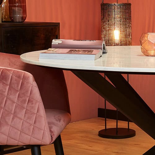 Prachtige moderne eettafel met een glanzende marmeren top en een zwart metalen onderstel, omgeven door een luxueus pastelroze velvet stoel, sfeervolle warme verlichting en stijlvolle decoratieve elementen, perfect voor een elegant interieur.