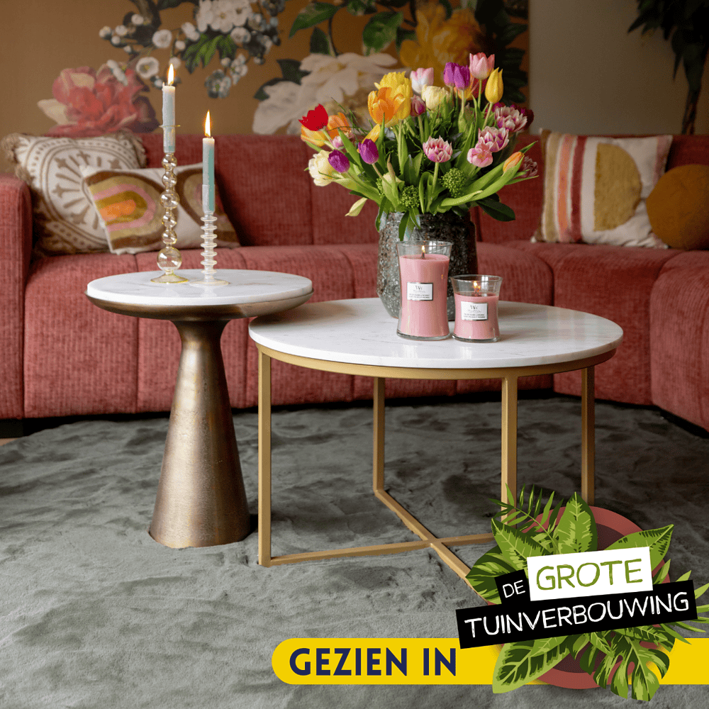 Elegant woonkamer met roze bank, houten en metalen salontafels, kleurrijke tulpen, en sfeervolle kaarsen, perfect voor een stijlvolle en gezellige interieurstijl.