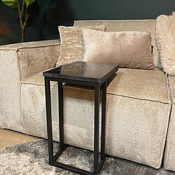 Stijlvolle zwarte bijzettafel met marmeren blad naast een beige stoffen bank, elegant interieur met zachte kussens en groene kamerplant op donkere muurachtergrond.