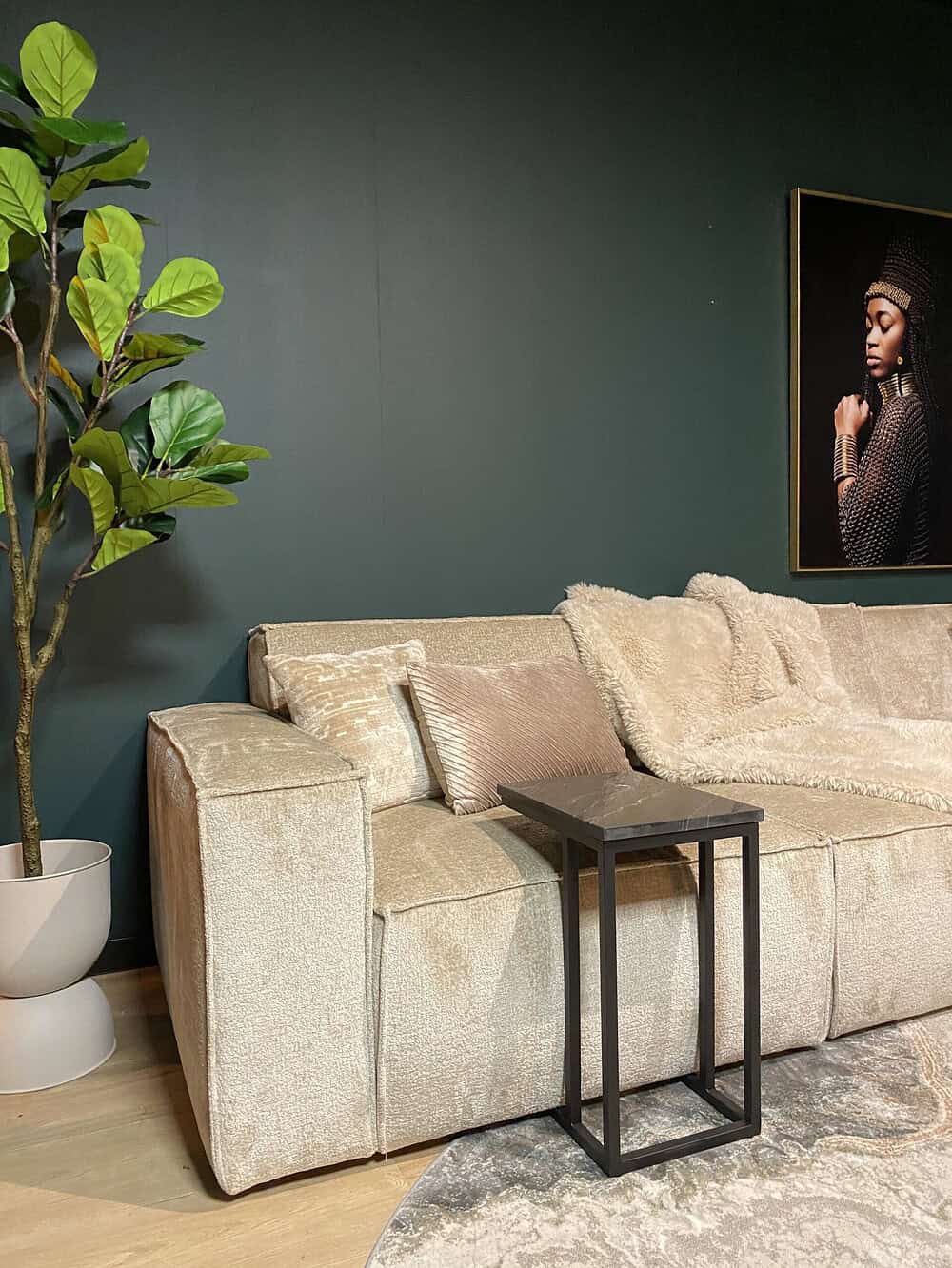 Luxueuze beige bank met zachte kussens en een modern zwart salontafeltje in een stijlvolle woonkamer met groene muur en kunstwerk.